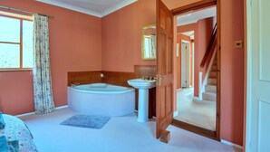 A bathroom with a bathtub, sink, and wooden door leading to a staircase. - Holiday Home in Mid Wales with Countryside Views (Llanidloes)