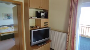 Een kamer met een bed, een televisie, houten kasten, een radiator en een raam met gordijnen.