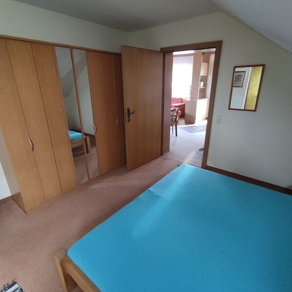A bedroom with a single bed, a wardrobe, and a door leading to another room.