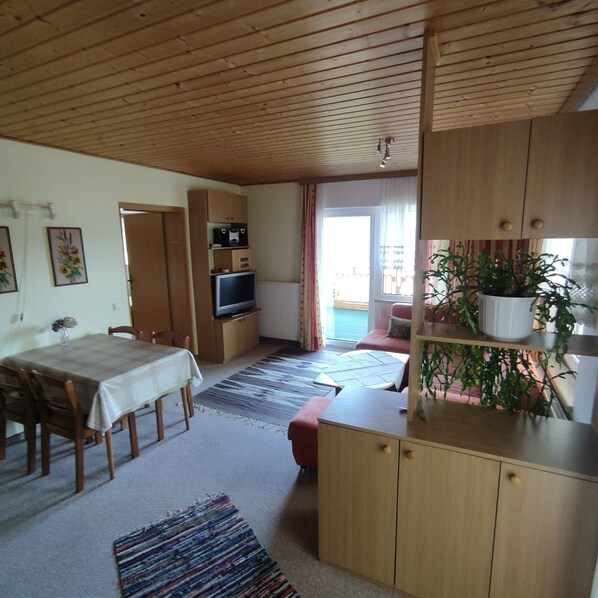 A cozy room with a dining table, chairs, a TV, a sofa, and a potted plant.