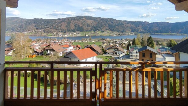 Een balkon met uitzicht op een meer, huizen en bergen.