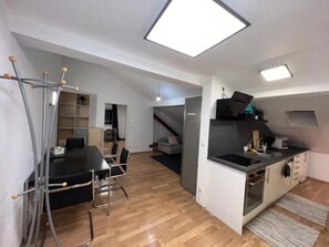 Una cocina moderna con una isla central, un comedor con mesa y sillas, y una escalera que sube a otro nivel.