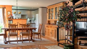A modern kitchen with wooden cabinets, a dining area with a table and chairs, and a television in a wooden entertainment unit. - Cottage in Bovey Tracey near Dartmoor Park (Bovey Tracey)