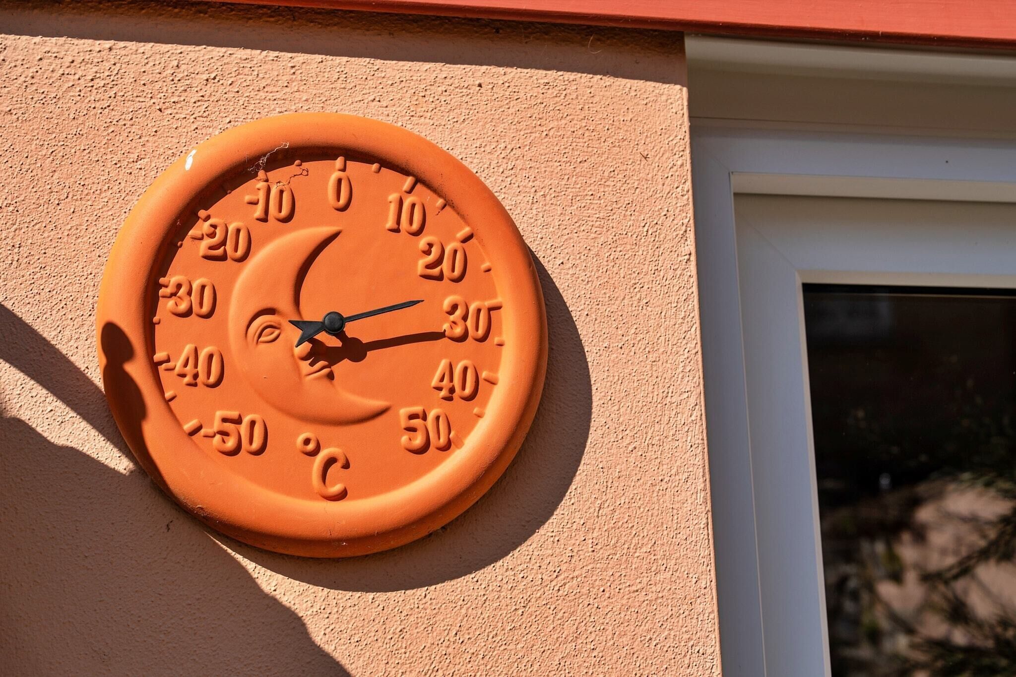 A round, orange outdoor thermometer mounted on a beige wall.