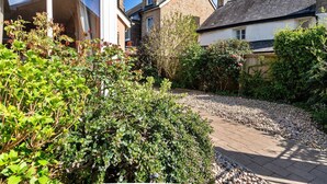 A residential garden with a paved pathway, dense greenery, and a house with a garage. - Cottage in Bovey Tracey near Dartmoor Park (Bovey Tracey)