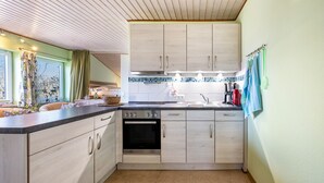 A kitchen with wooden cabinets, a built-in oven, a sink, and a window with curtains. - Apartment 'Fluss Aufwärts' with Private Terrace and Wi-Fi (Schülp)