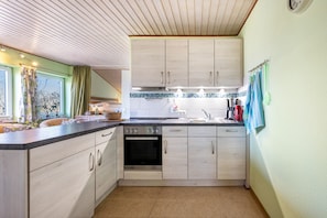 A kitchen with wooden cabinets, a built-in oven, a sink, and a window with curtains.