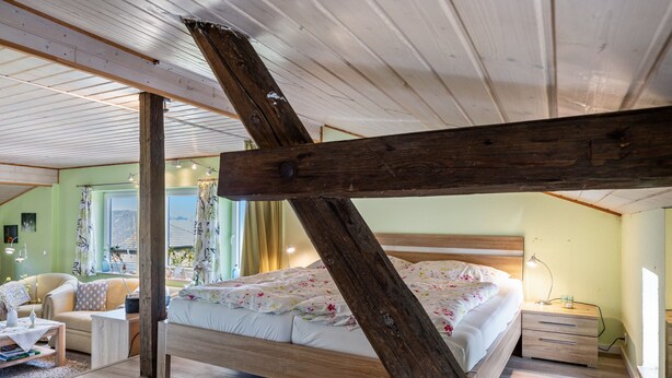 A bedroom with a wooden ceiling beam, a bed with floral bedding, a bedside table, and a chair. - Apartment 'Fluss Aufwärts' with Private Terrace and Wi-Fi (Schülp)