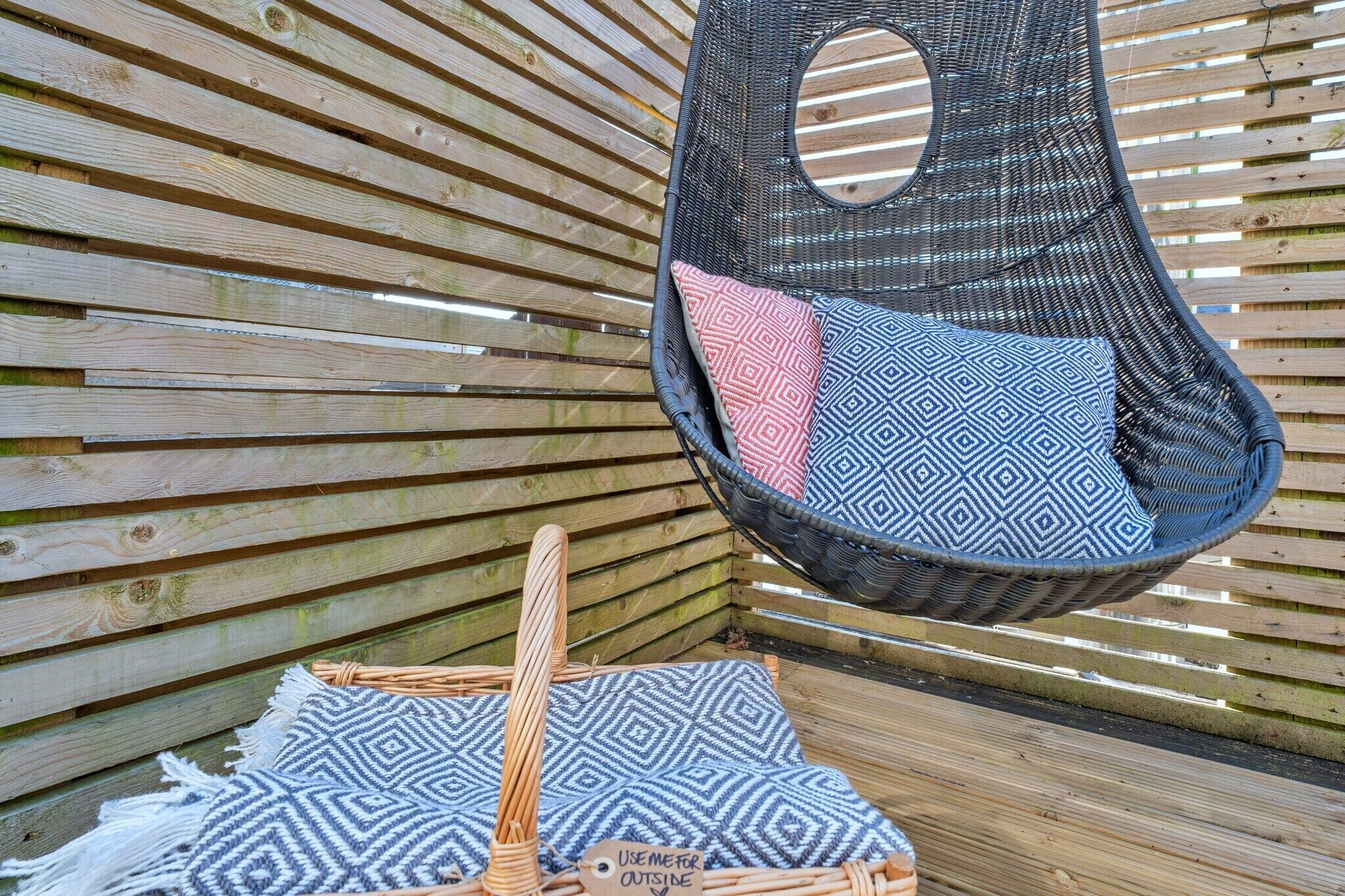 Une chaise en osier avec un coussin, un tapis tressé et un banc en bois.