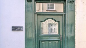 A green door with a small window above it and a sign reading "Yr Daflod" on the wall to the left.