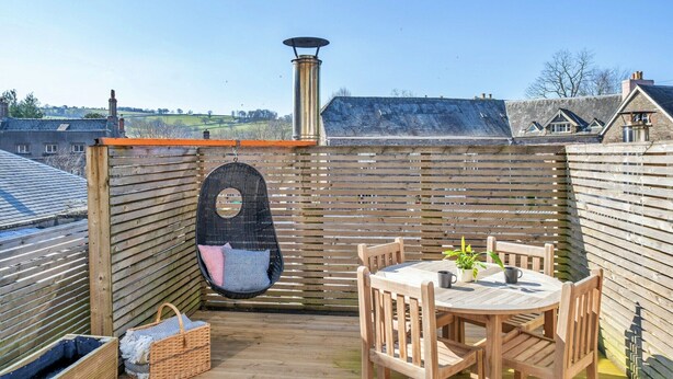 A wooden deck with a round table and chairs, a hanging chair, and a chimney.
