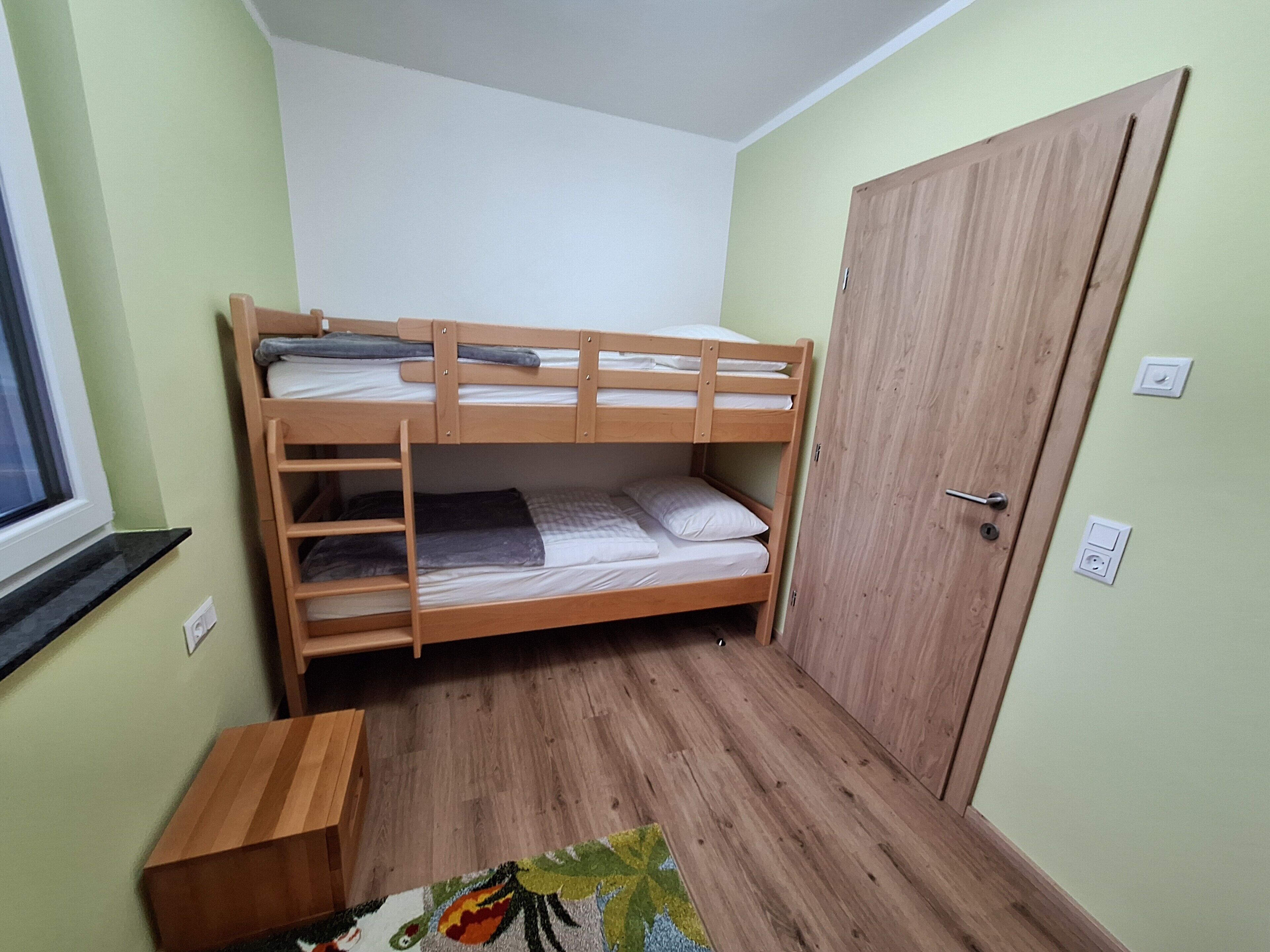 A bunk bed room with a wooden door, a small wooden table, and a window.