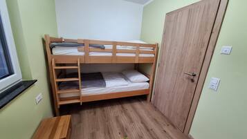 A bunk bed room with a wooden door, a small wooden table, and a window.