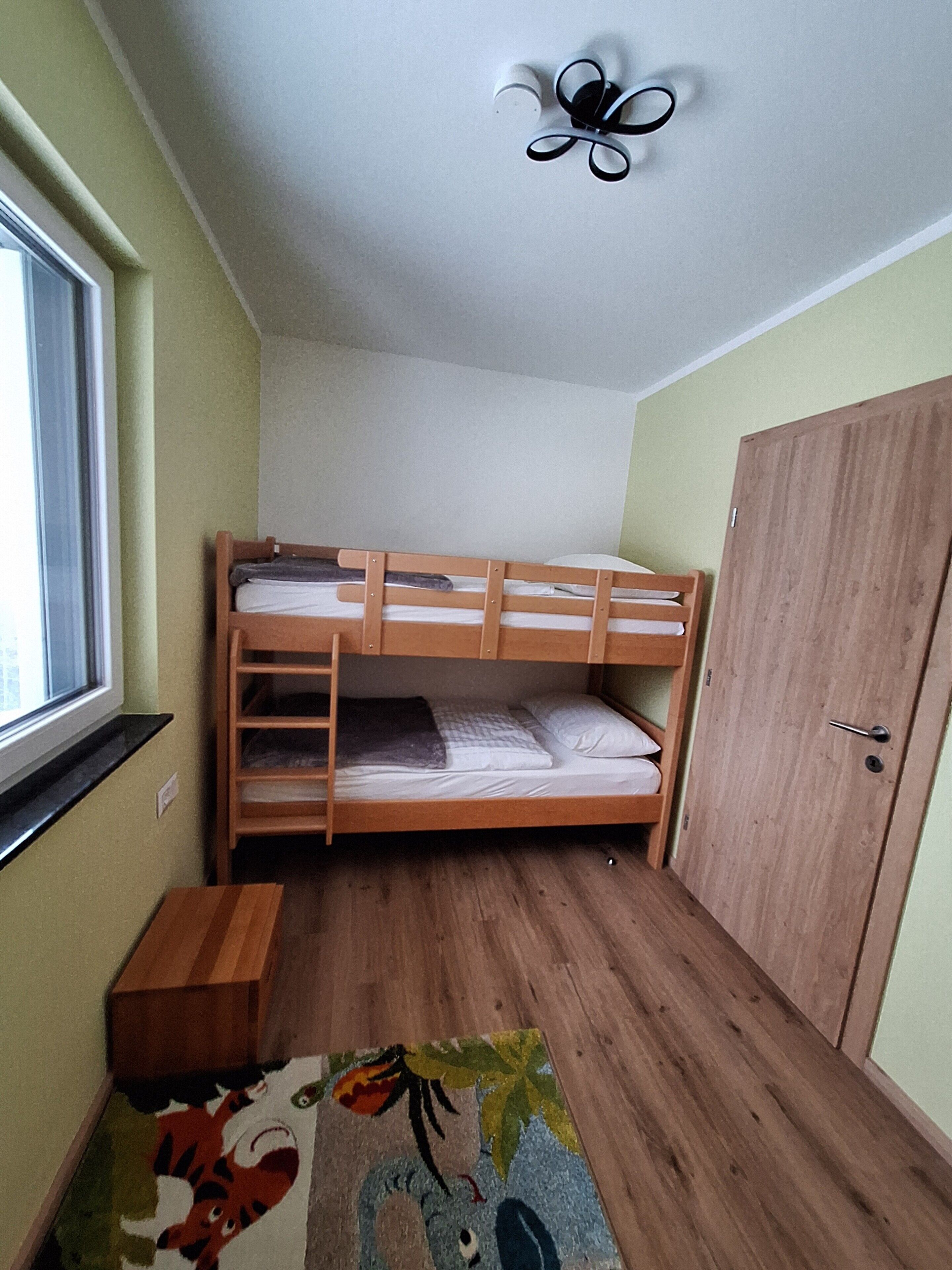 Una stanza con un letto a castello, un armadio, un tavolino e una finestra.