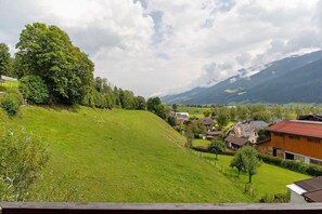 Une vue sur une colline, avec des maisons, un grand arbre et des montagnes en arrière-plan.