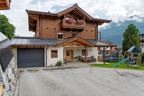 A wooden chalet with a balcony, a garage, and a playground.