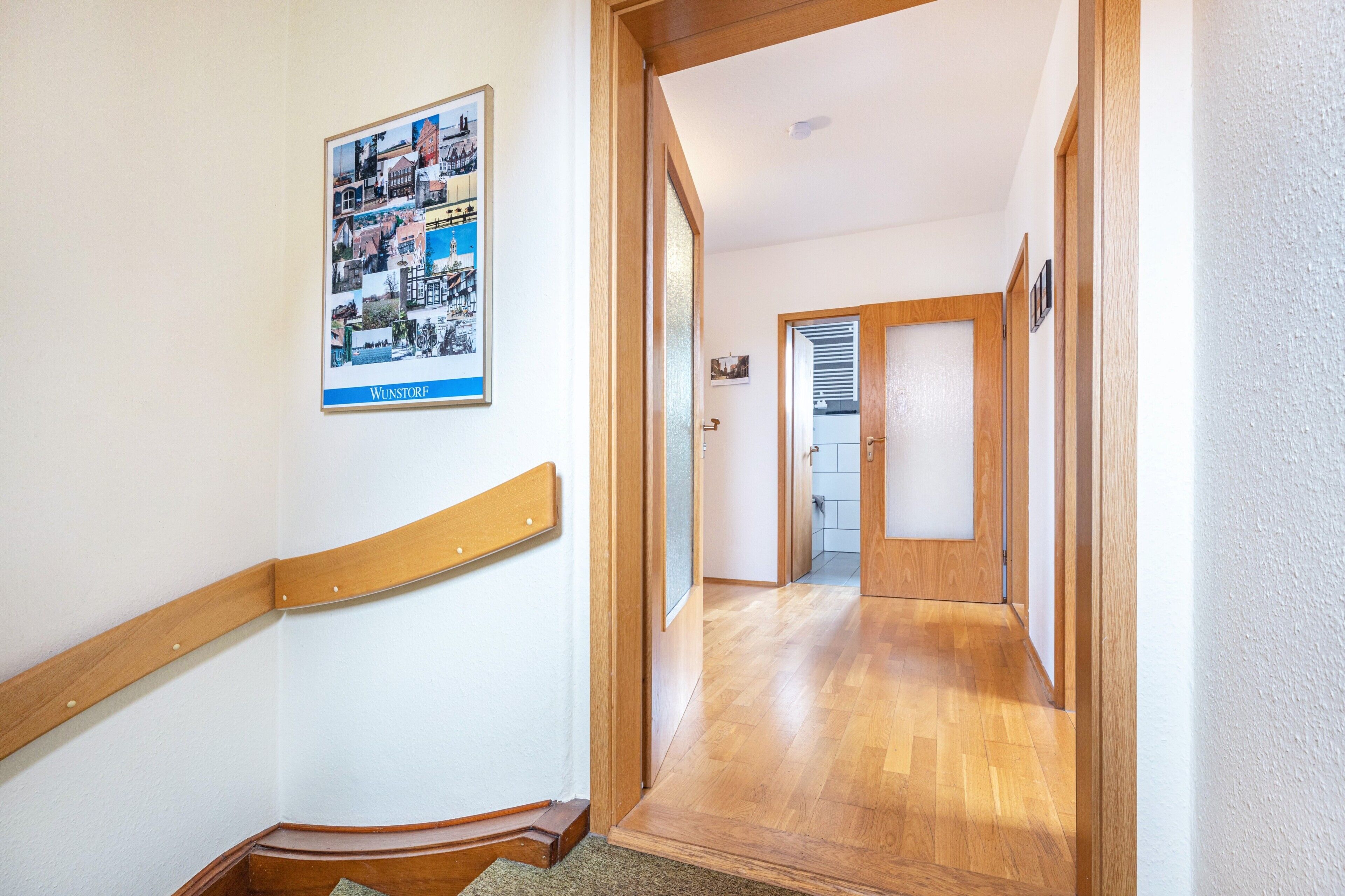 A hallway with wooden flooring, a wooden handrail, and a framed picture on the wall.