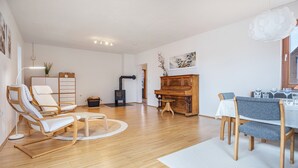 Uma sala de estar ampla com piso de madeira, um piano, uma mesa de jantar com cadeiras e uma lareira.