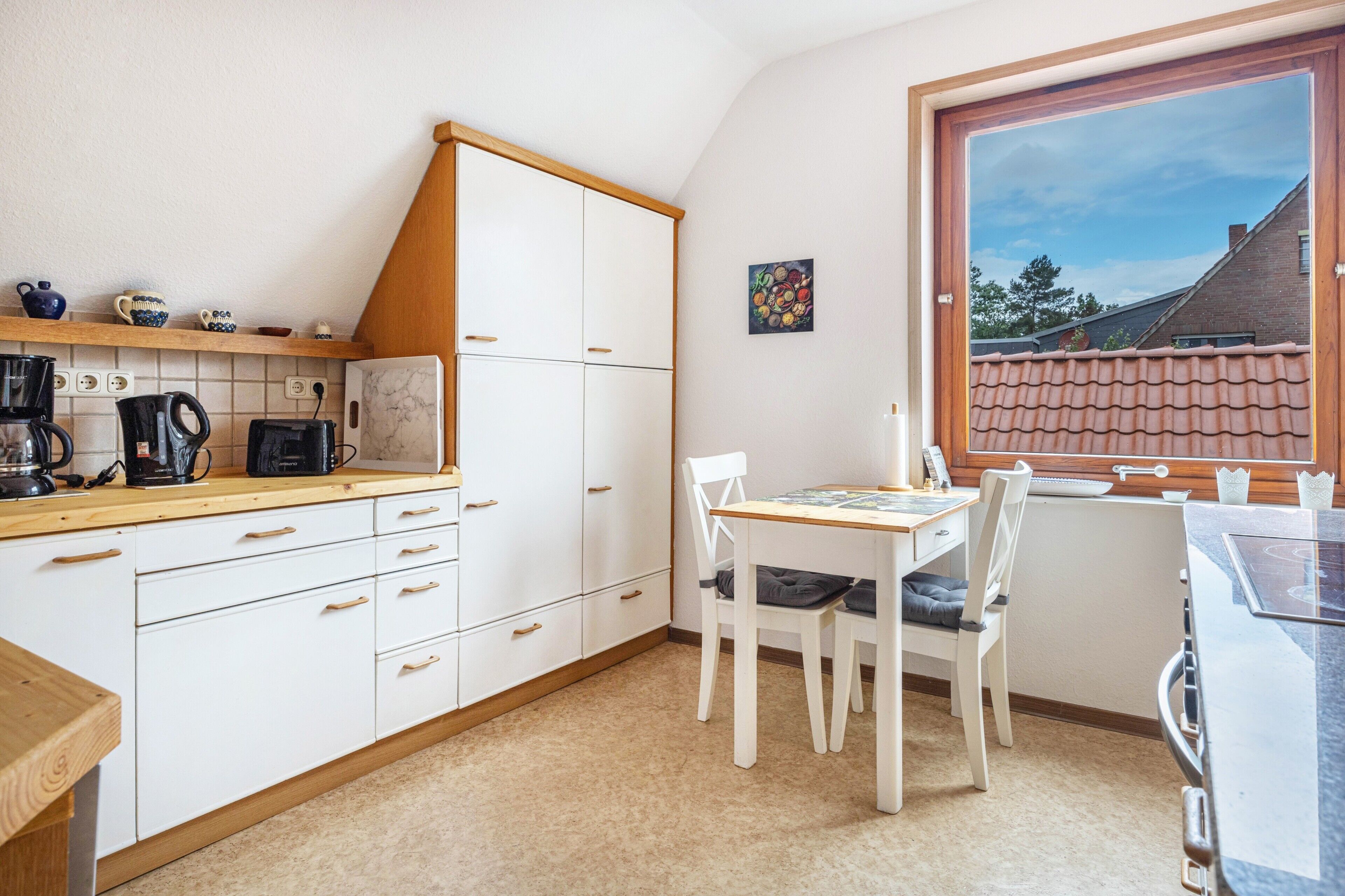 A kitchen with white cabinets, a wooden countertop, a dining table with chairs, and a window with a view of a house.