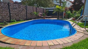 Une piscine avec un mur en pierre, de l’herbe et un escalier en métal.