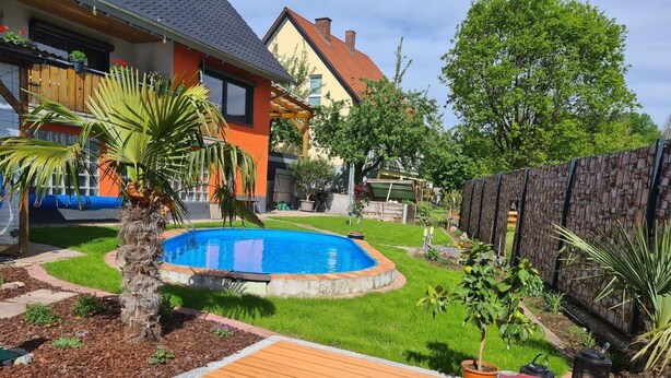 Un jardin avec une piscine, une terrasse en bois et une zone délimitée par une clôture.