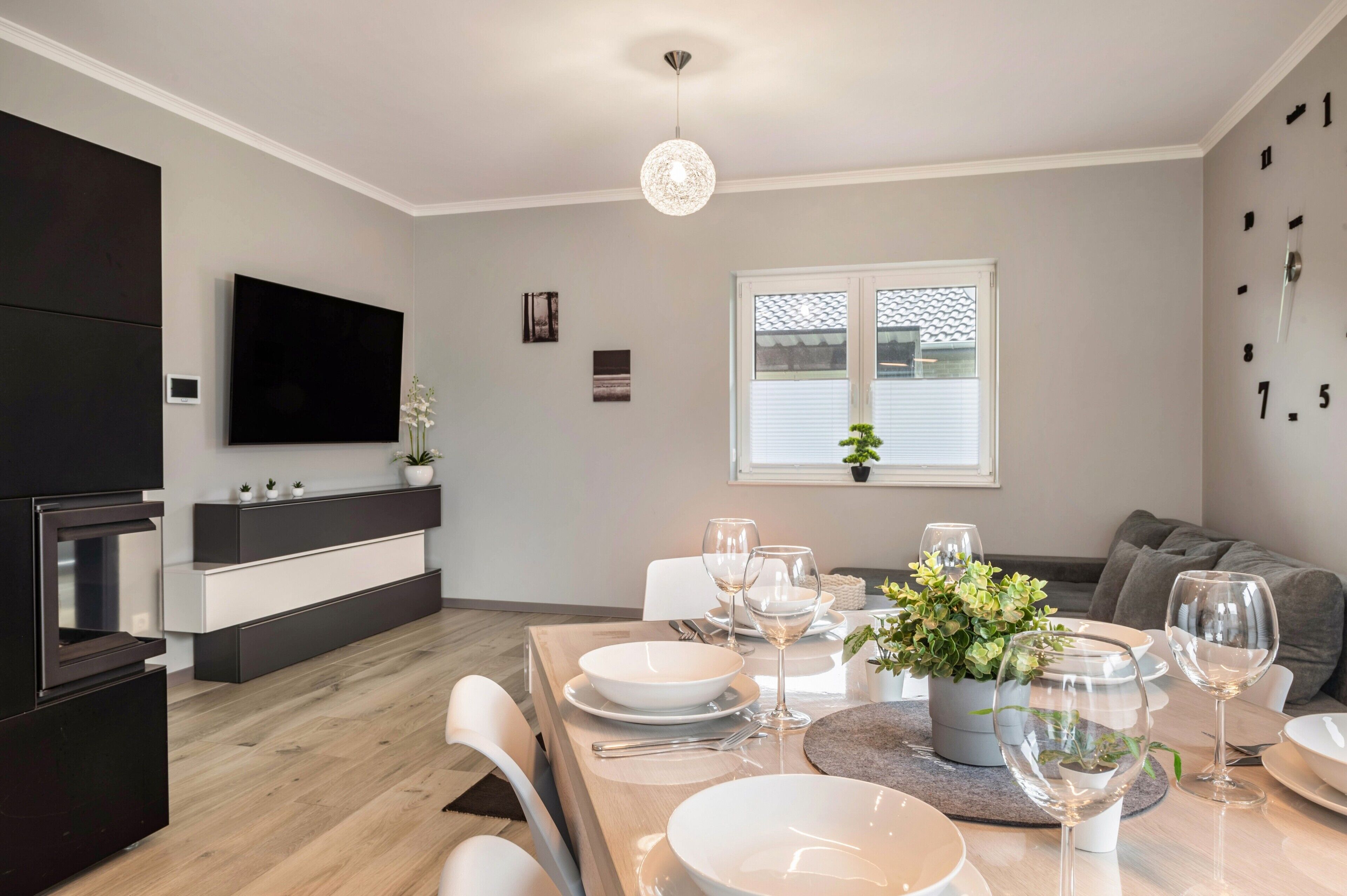 A modern kitchen with a flat-screen TV, built-in oven, and a dining area set for a meal with white plates, glasses, and a potted plant.
