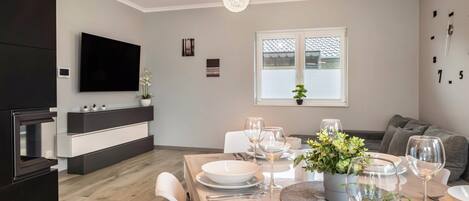 A modern kitchen with a flat-screen TV, built-in oven, and a dining area set for a meal with white plates, glasses, and a potted plant.