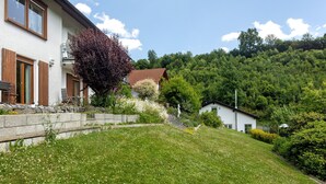 A two-story house with a balcony, a stone retaining wall, and a grassy slope.