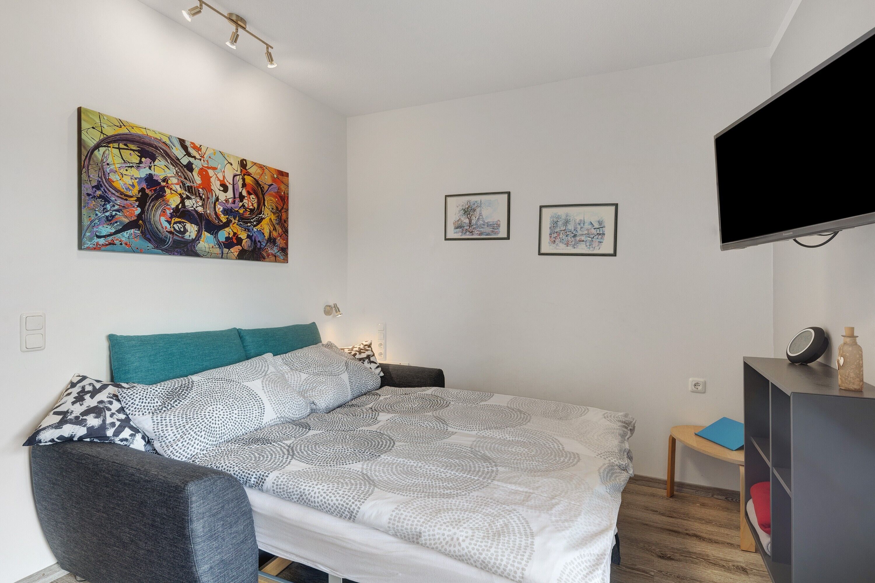 Ein modernes Schlafzimmer mit Bett, Fernseher, Gemälde und Schreibtisch.