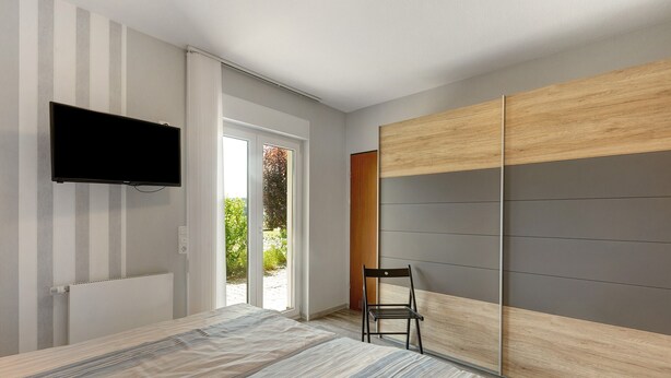 A bedroom with a bed, a TV, a sliding door, and a chair.