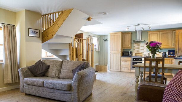 A modern kitchen with wooden cabinets, a dining area with a table and chairs, and a staircase leading to an upper level. - Cottage in Dee Valley near Castell Dinas Bran (Llangollen)