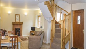 A living room with a fireplace, a dining table with chairs, a sofa, and a wooden staircase. - Cottage in Dee Valley near Castell Dinas Bran (Llangollen)