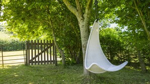 A hanging chair suspended from a tree in a grassy area with a wooden fence in the background. - Cottage in Dee Valley near Castell Dinas Bran (Llangollen)