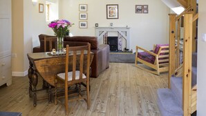 Un salon chaleureux avec une table à manger en bois, un canapé en cuir marron et un fauteuil à bascule en bois. On y trouve une cheminée avec une manteau de cheminée et des tableaux encadrés accrochés au mur.
