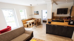A modern living room with a sofa, a coffee table, a dining area with a bench, and a kitchen with dark cabinets and a wooden countertop. - Apartment 'Alter Pferdestall' with Private Terrace and Wi-Fi (Meschede)