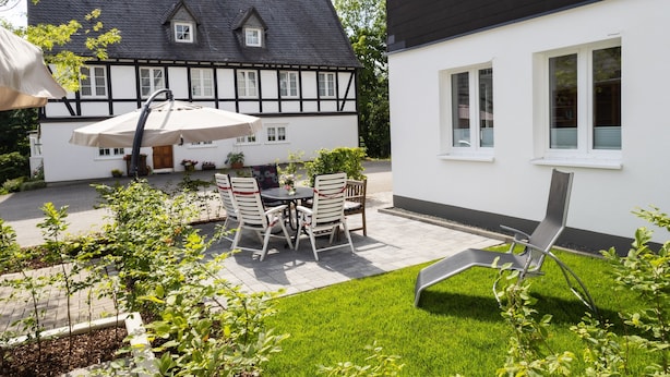 A courtyard with a table and chairs, a lawn, and a building with a black roof and white walls. - Apartment 'Alter Pferdestall' with Private Terrace and Wi-Fi (Meschede)