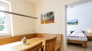 A room with a wooden dining table, chairs, a bed with a view, and a painting on the wall. - Apartment 'Alter Pferdestall' with Private Terrace and Wi-Fi (Meschede)