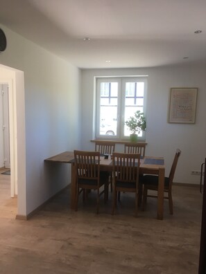 En matplats med ett bord och stolar, ett fönster med persienner och en växt på fönsterbrädan.
