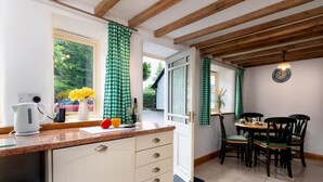Et køkken med træloft, et vindue med udsigt til grønne omgivelser, et spisebord med stole og en elkedel på bordet.