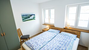 Een slaapkamer met een bed, een stoel, een bureau en een raam.