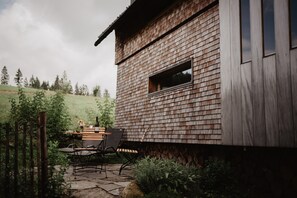 Un edificio rustico in legno con una finestra, un tavolo in pietra con sedie e un recinto di legno.