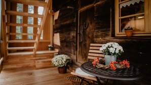 Una cabaña de madera con una escalera, una mesa con flores y una ventana con una planta.