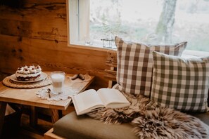 A cozy cabin interior with a wooden table, a cake, a glass of milk, a book, and checkered pillows. - Holiday Home 'Kornspeicher, 50qm' with Private Terrace, Private Garden and Wi-Fi (Titisee-Neustadt)