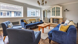 A living room with a fireplace, blue sofas, and a chandelier. - Cottage in Crimplesham with Games Room & Garden (Crimplesham)
