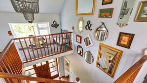 A multi-level interior with a wooden staircase, a chandelier, and various framed mirrors and pictures on the walls. - Cottage in Crimplesham with Games Room & Garden (Crimplesham)