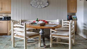 A dining area with a round wooden table, white chairs, and a wall-mounted clock. - Cottage in Crimplesham with Games Room & Garden (Crimplesham)