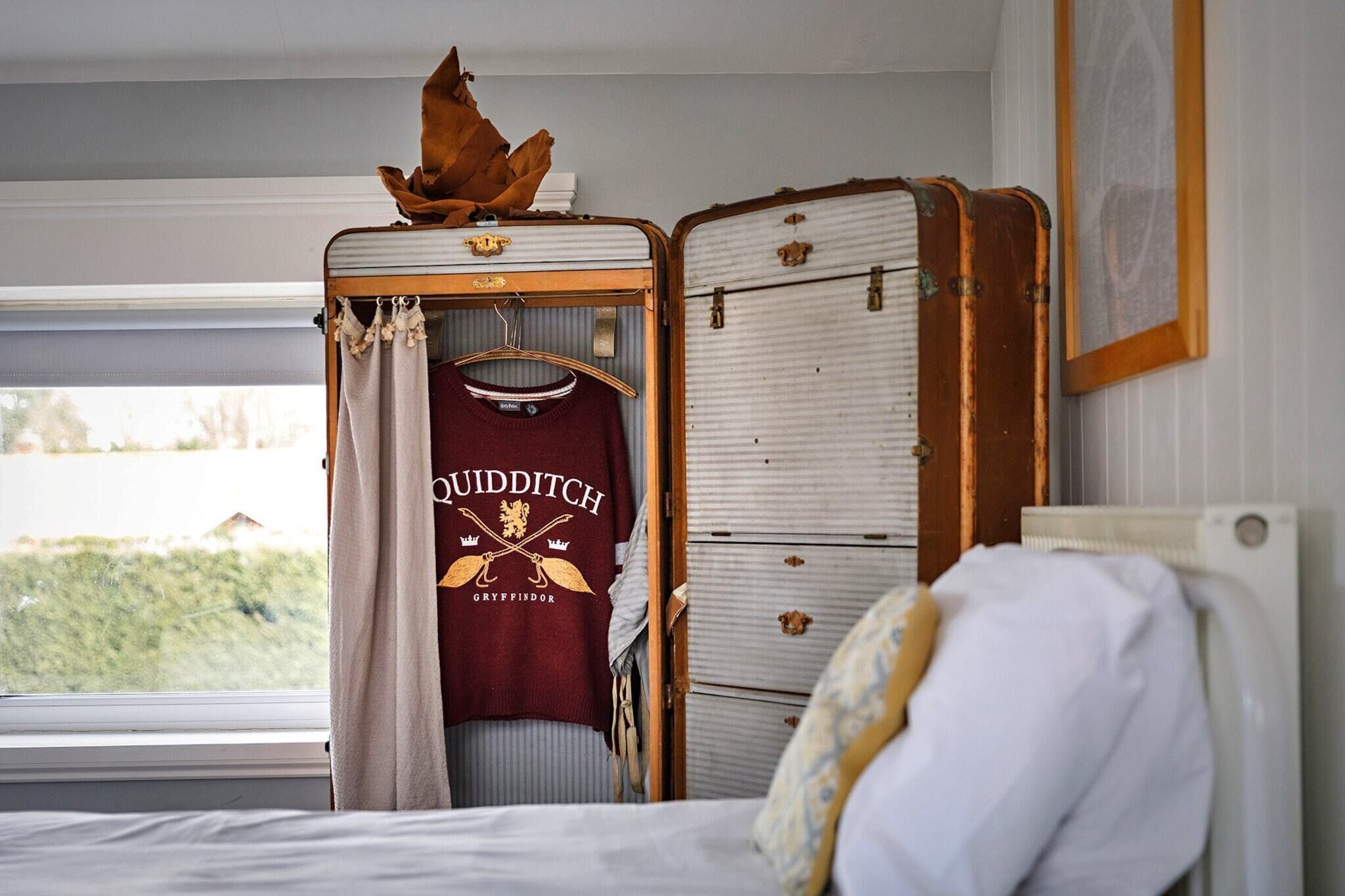 Un dormitorio con una cama, una maleta y una prenda colgada con la inscripción 'Gryffindor'.