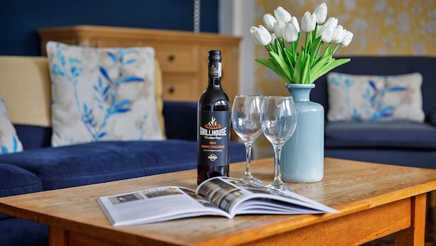 A wooden table with a bottle of wine, two glasses, and a vase of white tulips. - Cottage in Crimplesham with Games Room & Garden (Crimplesham)