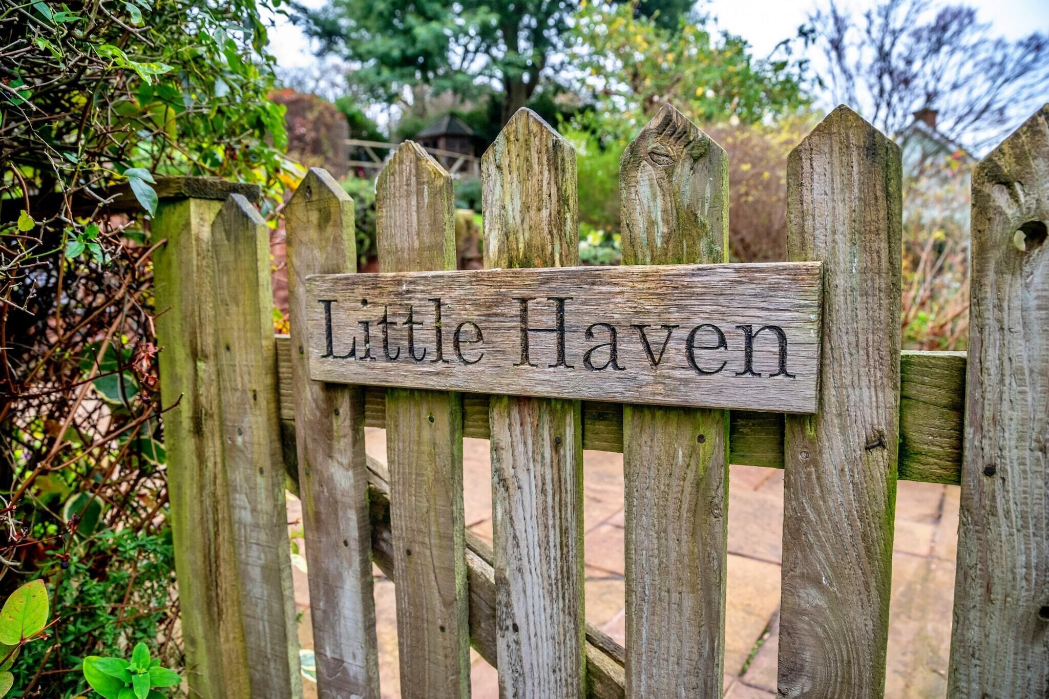 Une pancarte en bois portant l’inscription « Little Haven » est fixée à une clôture rustique.