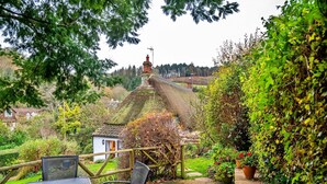 A garden patio with a table and chairs, surrounded by lush greenery and a view of a traditional house in the background. - Cottage in Alcombe near Exmoor Park (Alcombe)